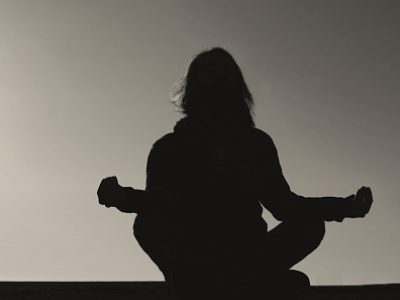 silhouette of a young man with long hair in meditation posture and sunset